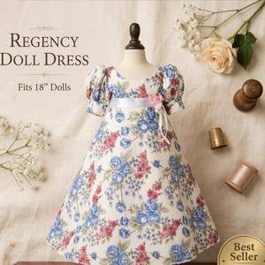 Könnte beinhalten: Ein Regency-Puppenkleid, passend für 45 cm große Puppen, wird auf einer Büste präsentiert. Das Kleid hat einen weißen Hintergrund mit einem Blumenmuster in Blau und Rosa. Es hat kurze Puffärmel und ein weißes Band in der Taille.