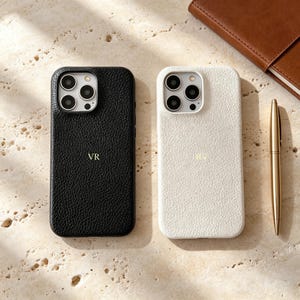 Può includere: Due cover per smartphone con finitura testurizzata e granulata, una nera e una bianca. Ogni cover presenta un ritaglio per la fotocamera a tripla lente e le iniziali VR impresse in oro al centro. Forma rettangolare con angoli arrotondati.