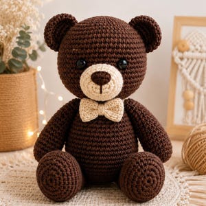 Puede incluir: Un oso de peluche tejido a ganchillo en color marrón oscuro con un hocico de color crema claro y una pajarita a juego. El oso tiene dos ojos negros redondos y una nariz bordada en marrón oscuro, con una textura de hilo en todo el cuerpo.