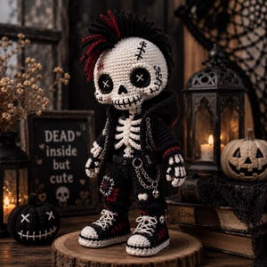 May include: A crocheted skeleton doll with black and red hair, wearing a black hooded jacket, trousers with patches, and high-top trainers. The doll features button eyes, a stitched mouth, and a silver chain accessory attached to the waistband.