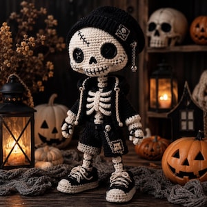 Puede incluir: Una muñeca esqueleto de ganchillo con un gorro negro con parche de calavera, sudadera con capucha negra y pantalones cortos negros. La muñeca tiene ojos de botón, detalles de boca cosidos y una pequeña cadena. Lleva zapatillas de ganchillo.