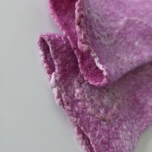 May include: Close-up of a felted textile in shades of purple. The fabric has a textured, slightly uneven surface with visible fibres. The edges are softly defined, with a lighter, almost white, border. The textile is folded, revealing its layered construction.