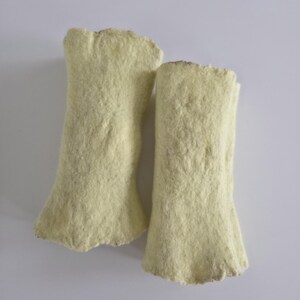May include: Two pale yellow, cylindrical objects with a dense, fibrous, and felted texture. Each piece has a slightly uneven, rough edge at the top and bottom, with a consistent, soft-looking surface throughout the length of both items.