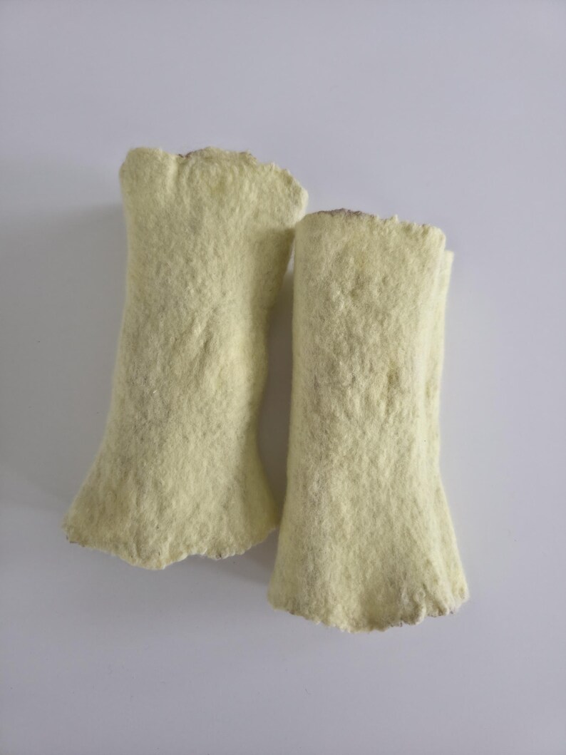May include: Two pale yellow, cylindrical objects with a dense, fibrous, and felted texture. Each piece has a slightly uneven, rough edge at the top and bottom, with a consistent, soft-looking surface throughout the length of both items.