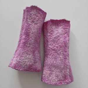 May include: A pair of magenta-coloured arm warmers made from a textured, felted material. The arm warmers have a flared shape at the wrist and a slightly ruffled edge. The background is plain white. The arm warmers are handmade.