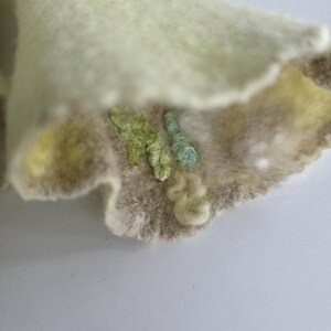 May include: A piece of light green felted fabric with a wavy, scalloped edge. The surface features textured embroidery in shades of light green, mint, and cream, with small, raised loops and tufts of fiber creating a tactile, dimensional pattern.