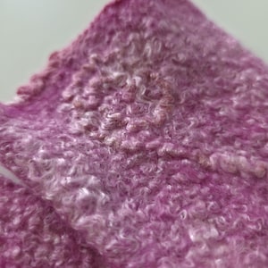 May include: Close-up of a textured, pink fabric with a curly, looped pattern. The fabric has a gradient effect, transitioning from a deep magenta to a lighter, almost white hue. The material appears soft and plush.