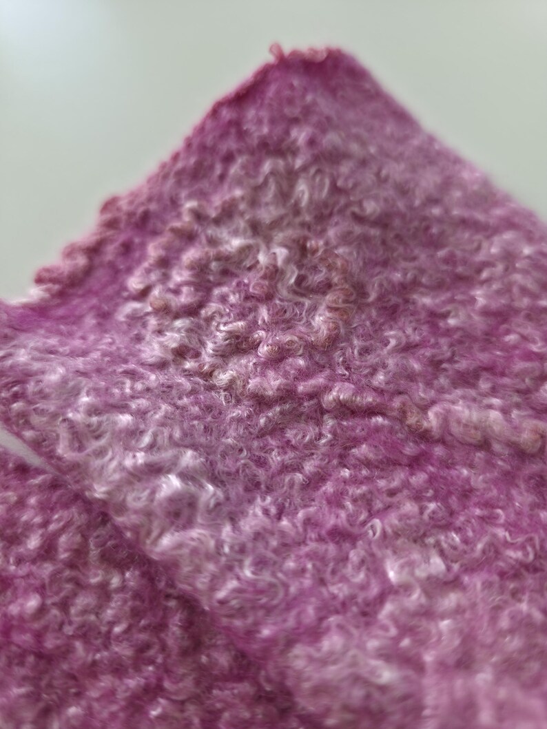 May include: Close-up of a textured, pink fabric with a curly, looped pattern. The fabric has a gradient effect, transitioning from a deep magenta to a lighter, almost white hue. The material appears soft and plush.