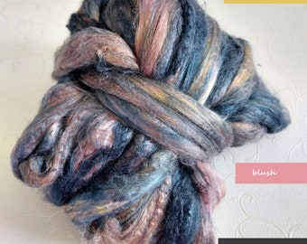 May include: A bundle of hand-dyed roving yarn in shades of dark gray, blush, and shooting star. The yarn is a mix of blues, pinks, and browns, with a soft, textured appearance. The labels read "shooting star", "blush", and "dark gray".