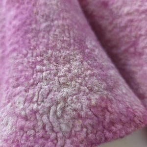 May include: Close-up of a textured, light purple fabric with a soft, fuzzy appearance. The fabric has a slightly uneven surface with variations in colour and texture, suggesting a natural material.