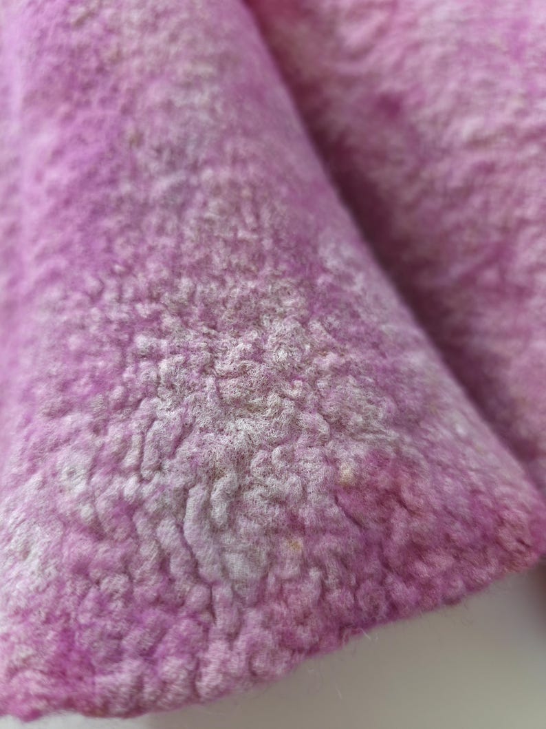 May include: Close-up of a textured, light purple fabric with a soft, fuzzy appearance. The fabric has a slightly uneven surface with variations in colour and texture, suggesting a natural material.