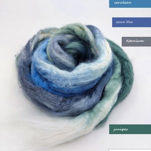 May include: A bundle of white, blue, and green merino wool roving. The colors are arranged in a gradient from white to cerulean blue to azure blue to titanium to juniper.