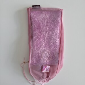 May include: A rectangular, pink, felted textile is encased in a sheer, light pink fabric pouch. The pouch has a drawstring closure and a small, square embellishment. The label at the top reads "Dante".