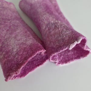 May include: A pair of magenta fingerless gloves, handmade from felted wool. The gloves have a textured finish and a ruffled edge at the wrist. They are designed to keep hands warm while allowing finger movement. The gloves are a vibrant shade of pink.