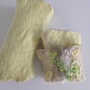 May include: Two pieces of felted wool. One is a long, pale yellow rectangular shape with a textured surface. The second piece is a shorter, light-colored rectangular cuff featuring intricate green and white embroidered floral details.