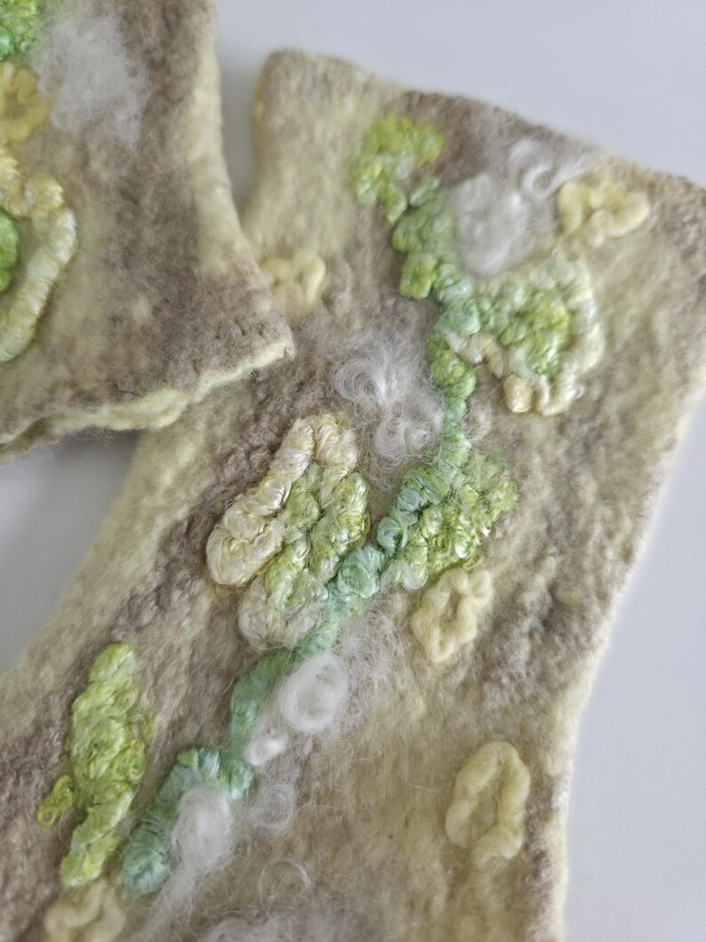 May include: Two rectangular felted wool pieces in shades of beige and cream, featuring raised, textured embroidery in light green, pale yellow, and white. The surface has a soft, fibrous appearance with organic, swirling patterns of stitched thread.