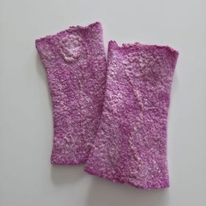 May include: A pair of handmade, fingerless gloves in a vibrant purple hue. The gloves feature a textured, felted wool design with a subtle floral embellishment near the wrist. The edges have a scalloped trim.