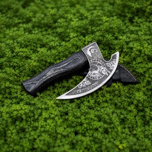 May include: A hand axe with a dark, wood-grained handle and a curved metal blade. The blade features an etched design of a raven within a circular border, accompanied by runic inscriptions and a small tree motif near the sharp, curved edge.