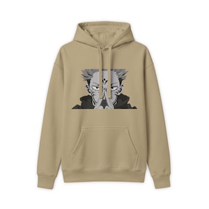 Peut inclure: Un sweat à capuche beige avec une impression graphique centrée représentant un personnage d'anime aux cheveux en pointe, avec des marques sur le visage et les mains jointes en prière. Le sweat possède une poche kangourou et des cordons assortis.