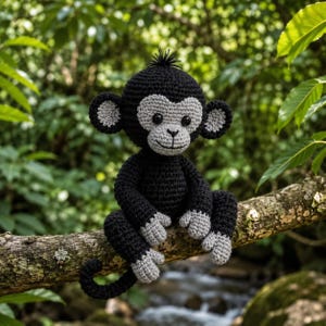 May include: A handmade crochet monkey in black and gray, perched on a tree branch. The monkey has a gray face, ears, hands, and feet, with a black body and a small tuft of hair on its head. The background features lush green foliage and a flowing stream.