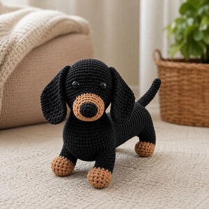 May include: A crocheted dachshund toy featuring a black body with tan accents on the paws and muzzle. The stuffed animal has two round black eyes, long floppy ears, and a short tail, crafted with a visible yarn texture throughout the entire figure.