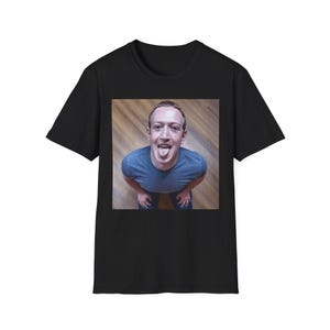 May include: A black short-sleeved t-shirt featuring a central square graphic print. The image displays a person wearing a blue t-shirt, looking upwards with their tongue sticking out, captured from a high-angle perspective against a wooden floor.