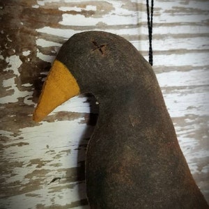 May include: A black felt bird ornament with a yellow beak and a black string for hanging. The bird has a stitched X on its head.