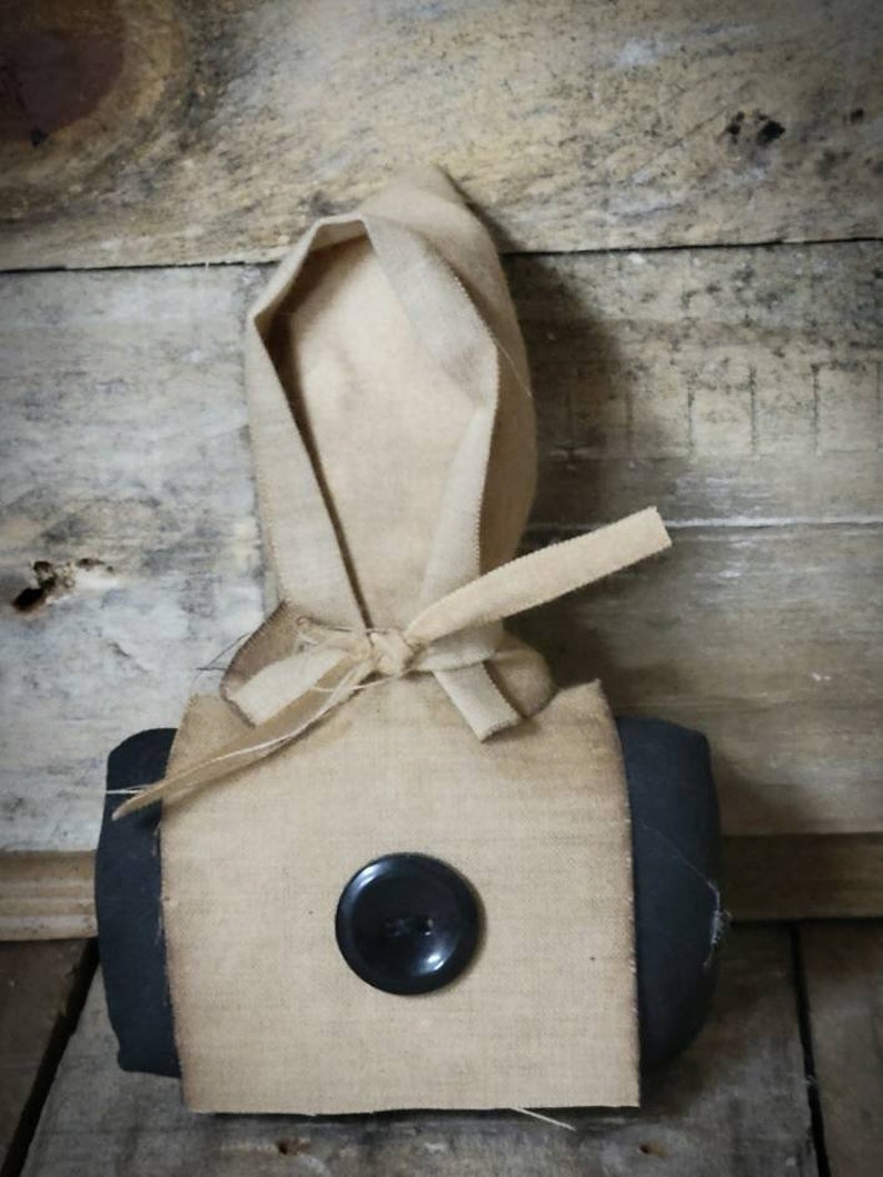 May include: A handmade fabric doll with a black button for an eye. The doll is wearing a brown fabric hood and a black fabric skirt.