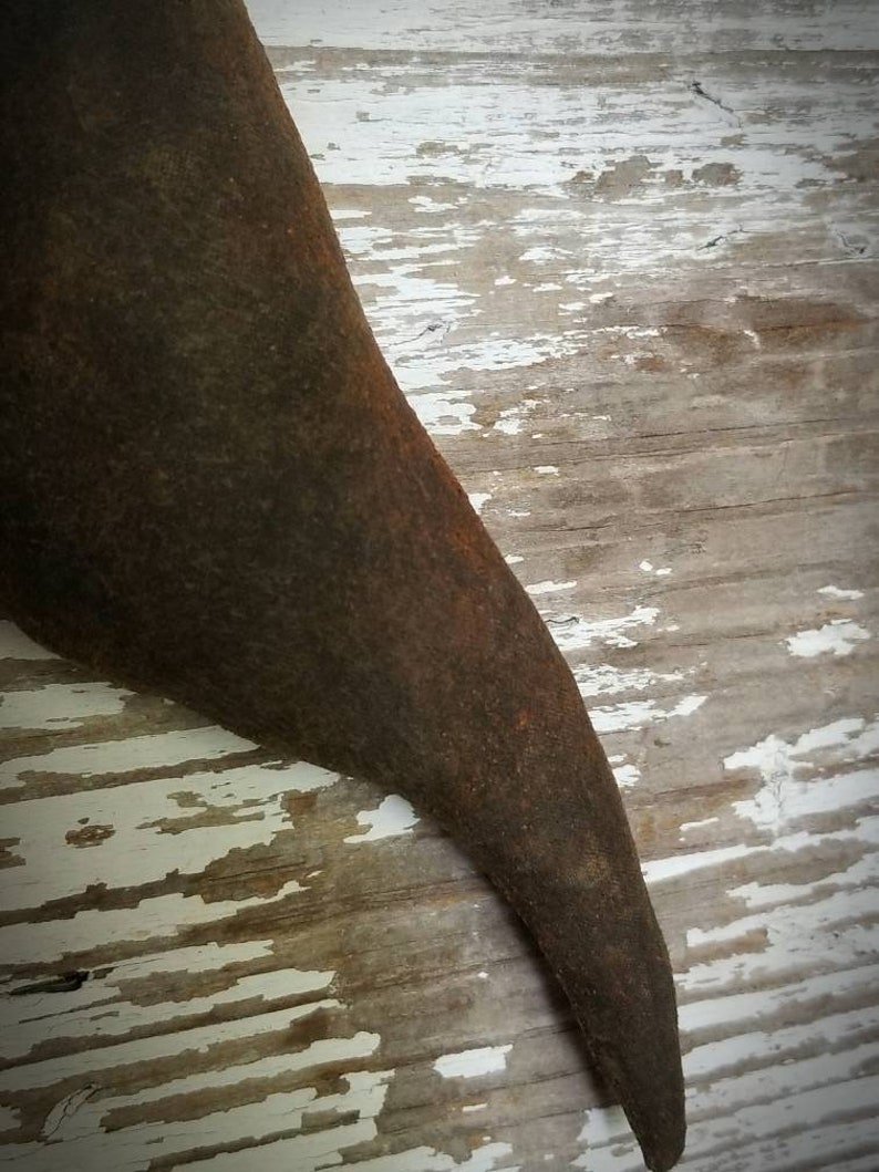 May include: A close-up of a dark brown, curved, metal object with a rough texture. The object is resting on a white and brown wooden surface.