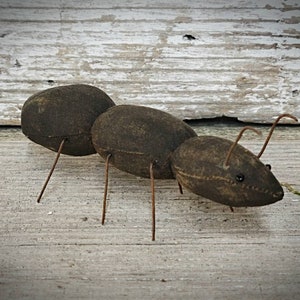Pu&ograve; includere: Una formica di stoffa marrone con gambe di filo metallico e occhi neri. La formica &egrave; in posa come se stesse camminando su una superficie di legno.
