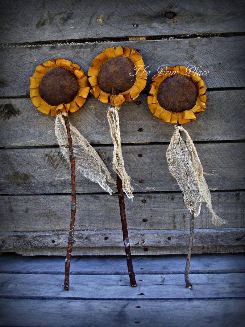 May include: Three rustic sunflower decorations with brown centers and yellow petals. The sunflowers are attached to brown sticks and have burlap fabric accents.