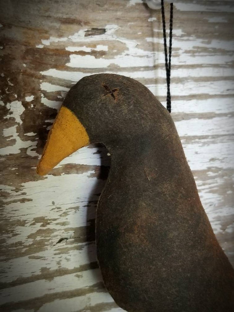 May include: A black felt bird ornament with a yellow beak and a black string for hanging. The bird has a stitched X on its head.
