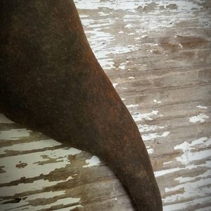 May include: A close-up of a dark brown, curved, metal object with a rough texture. The object is resting on a white and brown wooden surface.