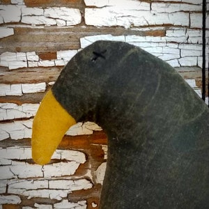 May include: A black and yellow fabric crow with a stitched X on its head. The crow is handmade and has a rustic, vintage look.