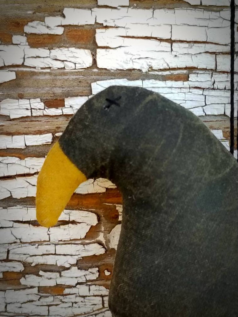 May include: A black and yellow fabric crow with a stitched X on its head. The crow is handmade and has a rustic, vintage look.