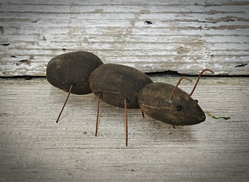 Pu&ograve; includere: Una formica di stoffa marrone con gambe di filo metallico e occhi neri. La formica &egrave; posizionata come se stesse camminando su una superficie di legno.