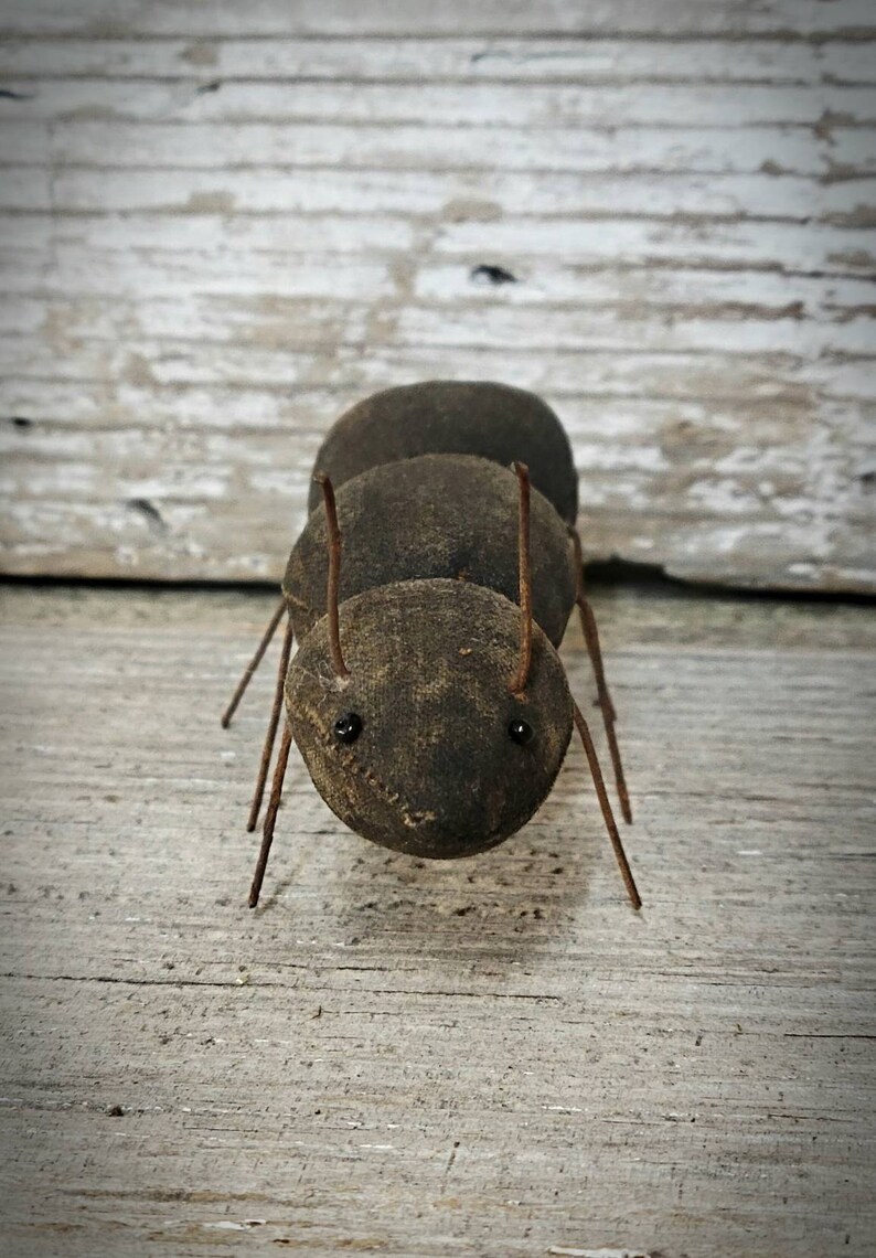 Pu&ograve; includere: Una formica marrone fatta a mano con gambe di filo metallico e occhi neri. La formica &egrave; fatta di tessuto e si trova su una superficie di legno.
