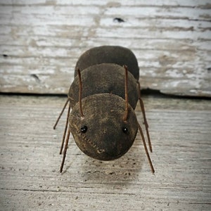 Pu&ograve; includere: Una formica marrone fatta a mano con gambe di filo metallico e occhi neri. La formica &egrave; fatta di tessuto e si trova su una superficie di legno.