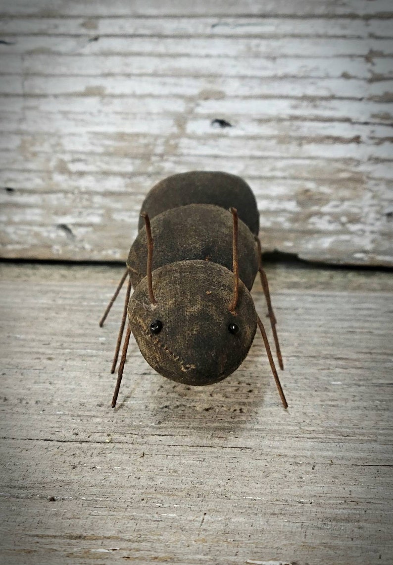 Pu&ograve; includere: Una formica marrone fatta a mano con gambe di filo metallico e occhi neri. La formica &egrave; fatta di tessuto e si trova su una superficie di legno.
