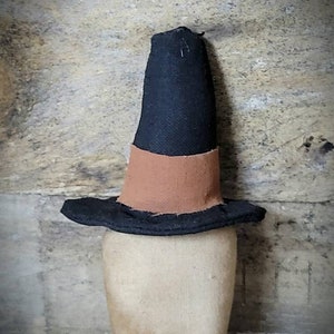 May include: A black witch's hat with a brown band. The hat is made of fabric and has a pointed top.
