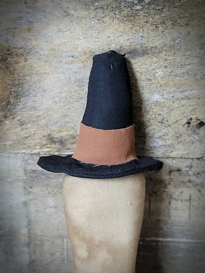 May include: A black witch's hat with a brown band. The hat is made of fabric and has a pointed top.