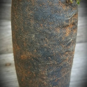 Op de afbeelding: Een donkergrijze keramische vaas met een ruw, getextureerd oppervlak. De vaas heeft een gespikkeld bruin glazuur en een afgeronde, cilindrische vorm.
