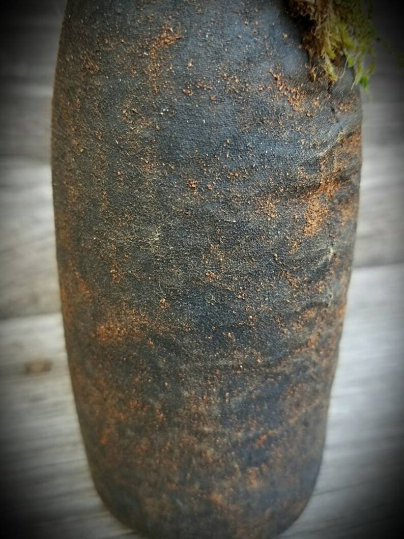 Op de afbeelding: Een donkergrijze keramische vaas met een ruw, getextureerd oppervlak. De vaas heeft een gespikkeld bruin glazuur en een afgeronde, cilindrische vorm.