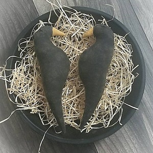 May include: Two black fabric birds with wooden beaks are nestled in a black bowl filled with straw.