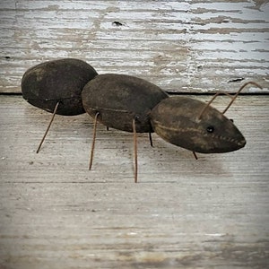 Pu&ograve; includere: Una formica di stoffa marrone con gambe di filo metallico. La formica &egrave; seduta su una superficie di legno marrone chiaro.