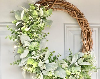May include: A green and white wreath made of faux greenery and vines. The wreath is hanging on a white door.