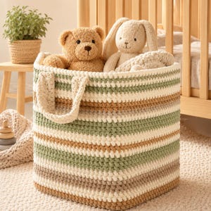 May include: A large, striped crochet storage basket in cream, green, and brown. Inside the basket are a brown teddy bear and a beige bunny plush toy. The basket has two cream handles and is on a cream rug. The basket is approximately 30 cm in height.