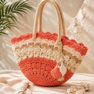 May include: A semi-circular crochet handbag featuring a scalloped pattern in alternating bands of coral, beige, and cream. The bag has two sturdy woven handles and a decorative charm consisting of a crocheted seashell and a leaf shape.