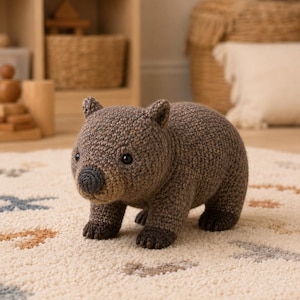 Op de afbeelding: Een gehaakt wombat knuffeldier in bruin met een donkergrijze neus en zwarte ogen. Het wezen staat in een staande positie en toont een gedetailleerde garentextuur over het hele lichaam, met donkerder bruin garen op de vier poten en oren.