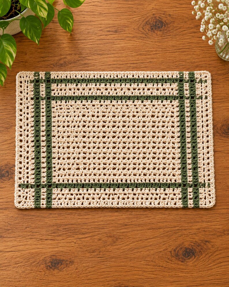 Op de afbeelding: Een rechthoekige gehaakte placemat met een cr&egrave;mekleurige basis en een rasterachtig patroon van donker bosgroen garen. Het ontwerp bestaat uit een centraal gedeelte met open steken, omlijst door dubbele verticale en horizontale groene strepen.